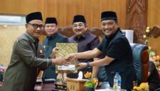 SINERGI EKSEKUTIF-LEGISLATIF: Bupati Tanjung Jabung Barat, Drs. H. Anwar Sadat, M.Ag. (kiri), menerima dokumen Pemandangan Umum Fraksi dari pimpinan DPRD dalam Rapat Paripurna LKPJ TA 2025 di Gedung DPRD Tanjab Barat, Senin (06/04). Sebanyak tujuh fraksi memberikan 
