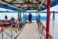 Kondisi halte penyeberangan atau dermaga apung di Desa Tanjung Senjulang, Kecamatan Bram Itam, Kabupaten Tanjung Jabung Barat, yang ambruk dan tenggelam sebagian ke dalam sungai. Sejumlah warga dan petugas tampak berada di lokasi jembatan penghubung untuk memantau situasi pasca-kejadian, Kamis (2/7). (Foto: Istimewa)