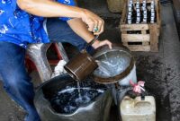 Ilustrasi aktivitas penuangan minyak tanah menggunakan takaran literan kaleng tradisional. Bahan bakar cair yang sangat akrab dengan generasi 1970-an ini kini kian langka dan transaksinya kerap dilakukan secara sembunyi-sembunyi oleh pedagang eceran karena terbentur regulasi HET dan aturan distribusi resmi Pertamina. (Foto: Ilustrasi/Media Online)