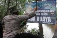 Anggota Polsek Tungkal Ilir danBabinsa Memasang Spanduk Imbau Warga Tak Mandi dan Bermain di Bantaran Sungai Bram Itam, Minggu (11/07/21).