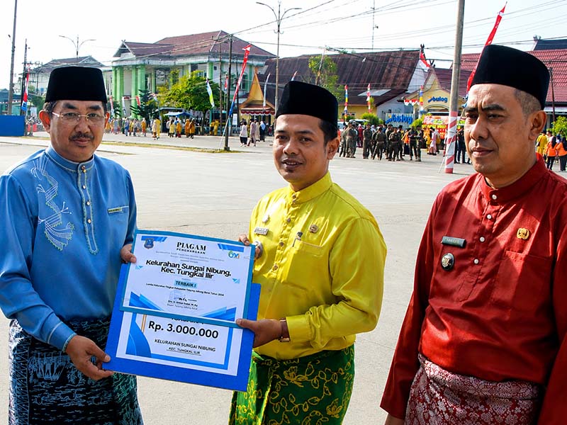 Bupati H. Anwar Sadat), menyerahkan piagam penghargaan dan dana pembinaan kepada Lurah Sungai Nibung Kecamatan Tungkal Ilir, Alfizan Fajri (tengah), sebagai Juara I Kelurahan Berprestasi Tingkat Kabupaten Tanjung Jabung Barat Tahun Anggaran 2026, Senin (10/08). (FOTO : Dok. Prokopim)