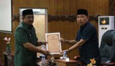 Bupati Tanjung Jabung Barat, Drs. H. Anwar Sadat, M.Ag. (kanan), menyerahkan Nota Pengantar Rancangan KUA-PPAS APBD Tahun Anggaran 2027 kepada Ketua DPRD Tanjab Barat, Hamdani, S.E. (kiri), dalam Rapat Paripurna di Ruang Rapat Utama DPRD, Senin (20/07). (Foto: Dok. Humas)