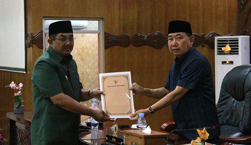Bupati Tanjung Jabung Barat, Drs. H. Anwar Sadat, M.Ag. (kanan), menyerahkan Nota Pengantar Rancangan KUA-PPAS APBD Tahun Anggaran 2027 kepada Ketua DPRD Tanjab Barat, Hamdani, S.E. (kiri), dalam Rapat Paripurna di Ruang Rapat Utama DPRD, Senin (20/07). (Foto: Dok. Humas)