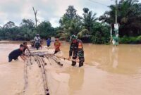 Gunakan Rakit Koptu Nurul Hidayat terobos banjir membantu warga melintasi Jalan terendam. FOTO : Dok/Babinsa