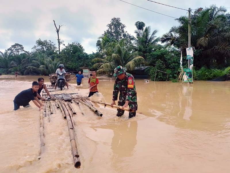 Gunakan Rakit Koptu Nurul Hidayat terobos banjir membantu warga melintasi Jalan terendam. FOTO : Dok/Babinsa