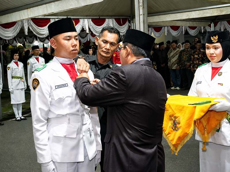 Bupati H. Anwar Sadat, menyematkan Lencana Merah Putih Garuda secara simbolis kepada pemimpin upacara dalam prosesi Pengukuhan 45 Anggota Pasukan Pengibar Bendera Pusaka (Paskibraka) Kabupaten Tanjung Jabung Barat Tahun 2026 di Halaman Rumah Dinas Jabatan Bupati, Sabtu (15/8/2026). (FOTO : Dok. Prokopim)