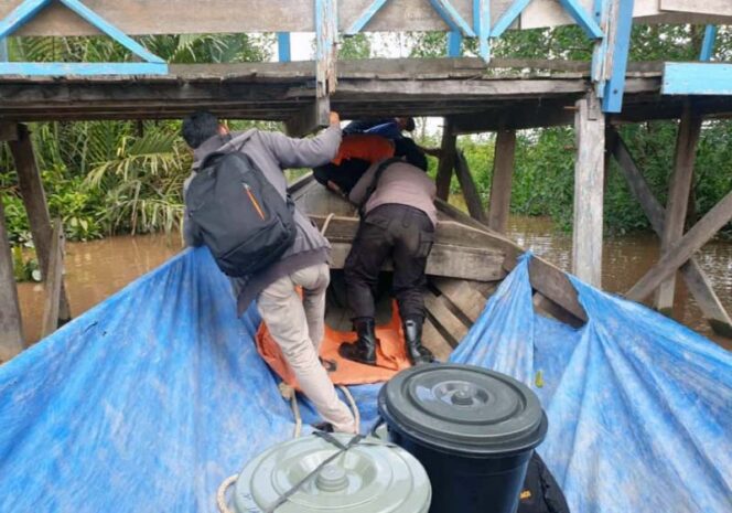 FOTO : Petugas Logistik Menunduk Melewati Kolong Jembatan yang Hampir Sangkut oleh Perahu Pompong di Salah Satu Desa di Kecamatan Pengabuan, Selasa (08/12/20).