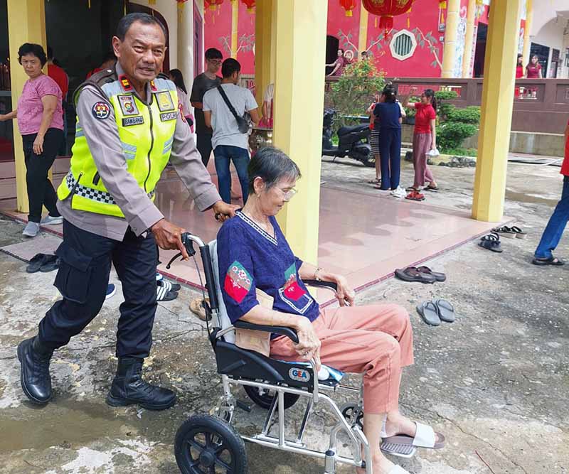 IPTU Bambang Wijarnako Mendorong Kursi Roda wanita tua yang duduk di kursi roda Menuju Vihara, Minggu (22/1/23). FOTO : Humas.