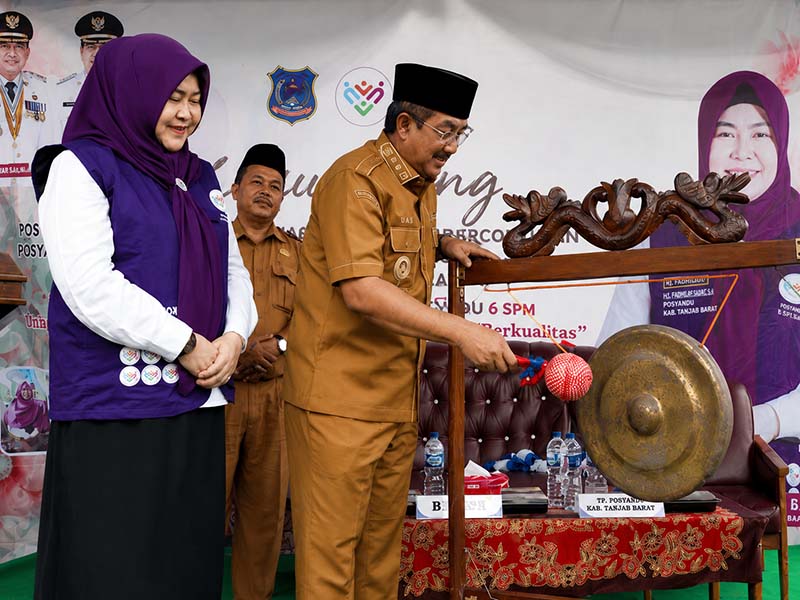 Bupati H. Anwar Sadat, didampingi Ketua Tim Pembina Posyandu Kabupaten Hj. Fadhilah Sadat, S.H., melakukan pemukulan gong sebagai tanda peluncuran Posyandu 6 Standar Pelayanan Minimal (SPM) Percontohan Cempaka II di Desa Pematang Lumut, Kecamatan Betara, Senin (6/7). (Foto: Diskominfo Tanjab Barat)