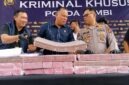 Direktur Reserse Kriminal Khusus (Dirreskrimsus) Polda Jambi, Kombes Pol Taufik Nurmandia (tengah), bersama Kabid Humas Polda Jambi, Kombes Pol Erlan Munaji (kanan), menunjukkan sebagian barang bukti uang tunai senilai Rp18,9 miliar yang berhasil disita dan dibekukan dari jaringan peretas internasional pembobol 6.609 rekening nasabah Bank Jambi, dalam konferensi pers di Mapolda Jambi, Selasa (14/7/2026). (FOTO : Dok. Kompas.com)