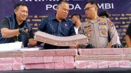 Direktur Reserse Kriminal Khusus (Dirreskrimsus) Polda Jambi, Kombes Pol Taufik Nurmandia (tengah), bersama Kabid Humas Polda Jambi, Kombes Pol Erlan Munaji (kanan), menunjukkan sebagian barang bukti uang tunai senilai Rp18,9 miliar yang berhasil disita dan dibekukan dari jaringan peretas internasional pembobol 6.609 rekening nasabah Bank Jambi, dalam konferensi pers di Mapolda Jambi, Selasa (14/7/2026). (FOTO : Dok. Kompas.com)