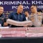 Direktur Reserse Kriminal Khusus (Dirreskrimsus) Polda Jambi, Kombes Pol Taufik Nurmandia (tengah), bersama Kabid Humas Polda Jambi, Kombes Pol Erlan Munaji (kanan), menunjukkan sebagian barang bukti uang tunai senilai Rp18,9 miliar yang berhasil disita dan dibekukan dari jaringan peretas internasional pembobol 6.609 rekening nasabah Bank Jambi, dalam konferensi pers di Mapolda Jambi, Selasa (14/7/2026). (FOTO : Dok. Kompas.com)