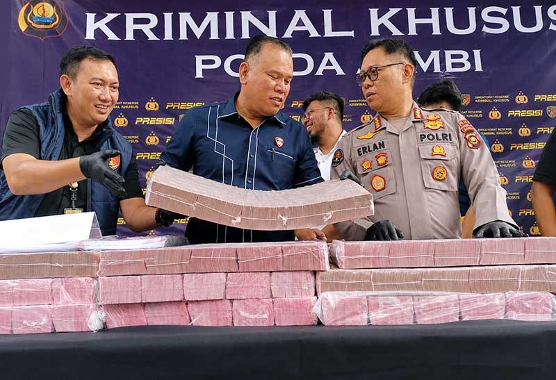 Direktur Reserse Kriminal Khusus (Dirreskrimsus) Polda Jambi, Kombes Pol Taufik Nurmandia (tengah), bersama Kabid Humas Polda Jambi, Kombes Pol Erlan Munaji (kanan), menunjukkan sebagian barang bukti uang tunai senilai Rp18,9 miliar yang berhasil disita dan dibekukan dari jaringan peretas internasional pembobol 6.609 rekening nasabah Bank Jambi, dalam konferensi pers di Mapolda Jambi, Selasa (14/7/2026). (FOTO : Dok. Kompas.com)