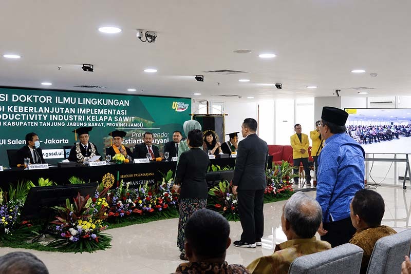 Bupati H. Anwar Sadat, (berdiri mengenakan kemeja batik biru dan peci hitam), menghadiri Sidang Terbuka Promosi Doktor Estiarty Haryani, S.Pt., M.T., di Kampus Universitas Indonesia, Salemba, Jakarta Pusat, Sabtu (4/7). Dalam sidang tersebut, Estiarty mempertahankan disertasinya yang meneliti strategi produktivitas hijau (green productivity) industri kelapa sawit dengan lokus penelitian di Kabupaten Tanjung Jabung Barat, Jambi. (Foto: Dok. Prokopim Tanjabbar)